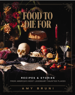 A macabre display of edible treats, black candlesticks, and a human skull lie atop a table on the cover of Food to Die For by Ami Bruni.