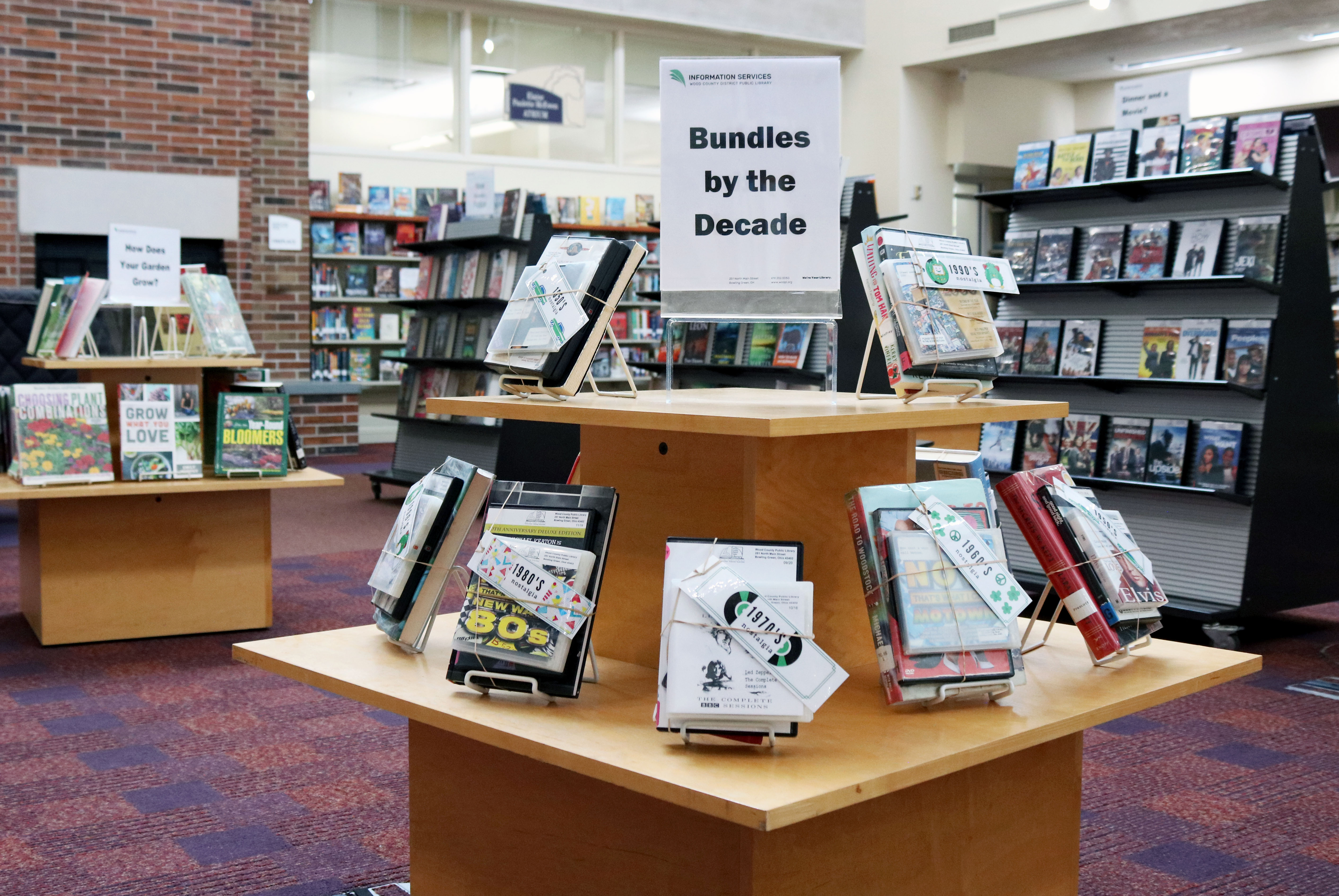 A library book stand with decade bundles of books, movies, and music from different decades