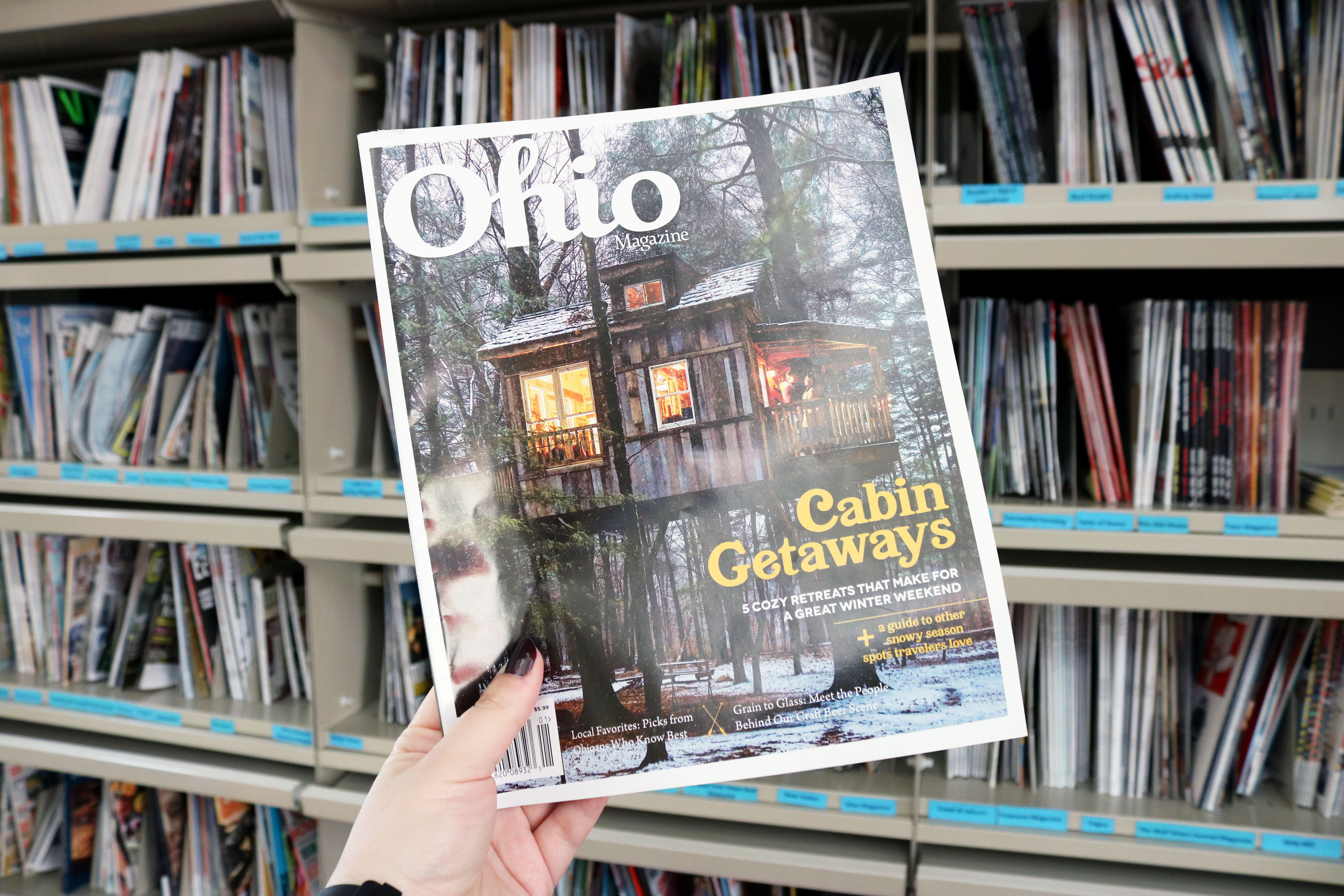 A hand holding an Ohio Magazine with magazines in the background